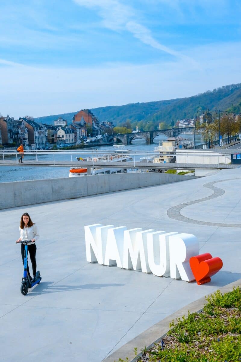 Femme à trottinette à côté du logo Namur